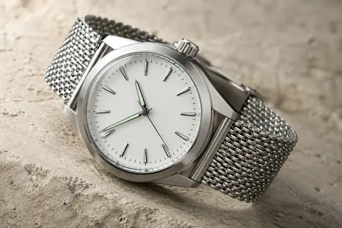 Montre automatique à cadran blanc, boîtier argenté et bracelet tressé en acier sur fond minéral ivoire.
