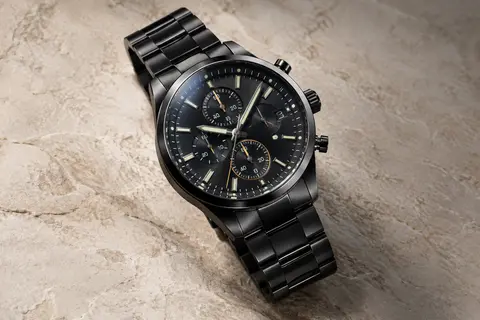 Montre chronographe Megalith à bracelet en acier noir, photographiée sur un fond minéral ivoire.