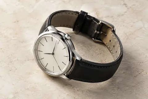Montre automatique au cadran blanc antique, boîtier argenté et bracelet en cuir noir sur fond minéral ivoire.