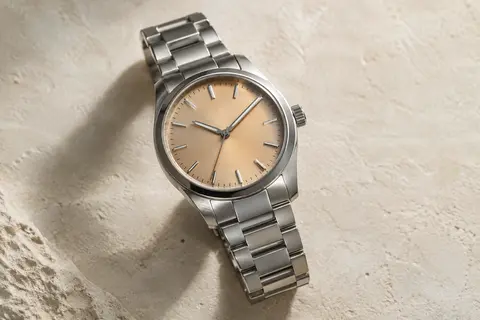 Montre automatique Orient au boîtier rond en acier argenté et au coloris beige, posée sur un fond minéral ivoire.